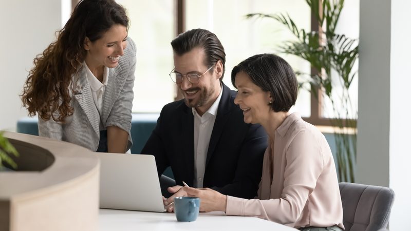 Three colleagues reviewing work together around a laptop in a bright office.